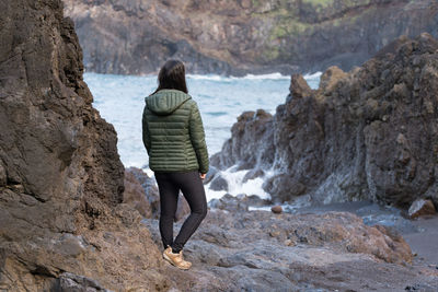 Rear view of man standing on rock by sea
