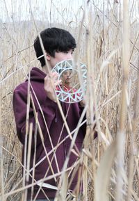 Boy holding mirror with friend reflection standing amidst plants on land