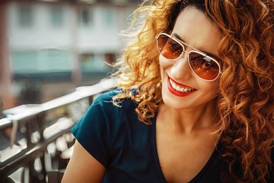 Smiling young moroccan woman, with curly brown hair, sitting in a cafe in mainz, wearing sunglasses