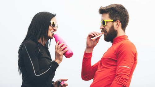 Side view of smiling couple eating food standing against white background