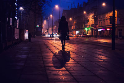 Rear view of silhouette woman walking on footpath in city at night