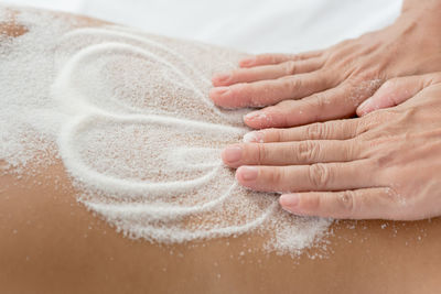 Cropped hands of massage therapist applying talcum powder on woman back