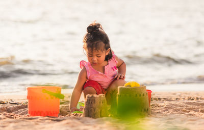 Happy fun asian child cute little girl playing sand with toy sand tools at a tropical sea beach