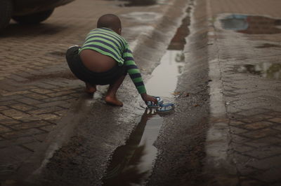 Rear view of boy by puddle on footpath
