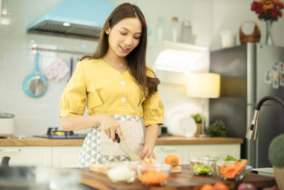 Smiling young woman preparing food in kitchen at home