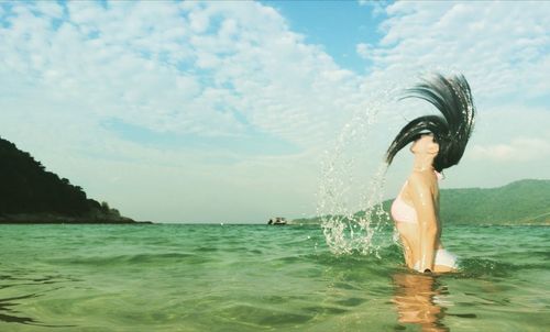 Woman tossing hair while standing in sea against sky