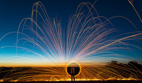 Rear view of man spinning wire wool against sky during sunset