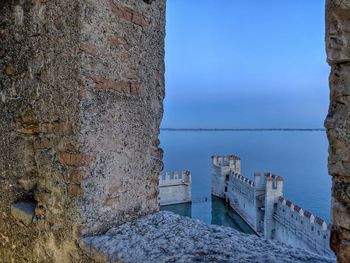 Old wall by sea against clear blue sky