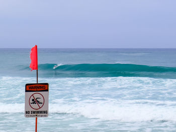 Warning sign on sea against sky