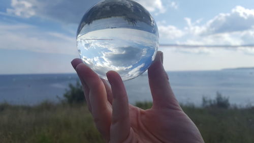 Close-up of hand holding crystal ball against sky