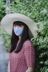 Portrait of woman wearing hat standing against plants