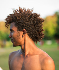 Shirtless man with curly hair against trees