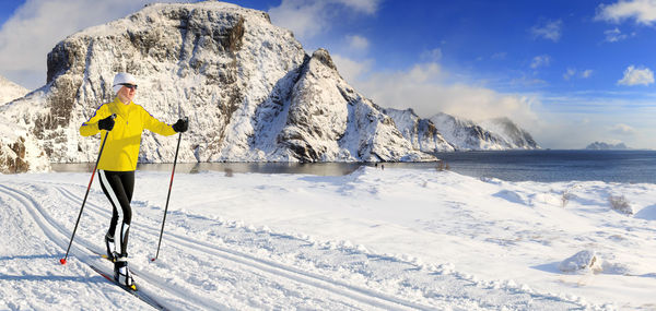 Mature woman skiing on snow covered field by sea and lake