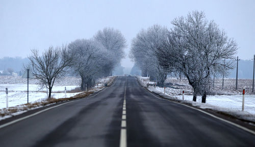 Road amidst bare trees against clear sky during winter