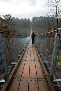 Rear view of man standing on footbridge against sky