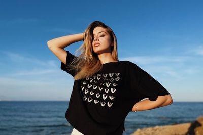 Young woman standing at beach against sky