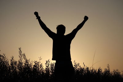Silhouette man standing by plants against sky during sunset