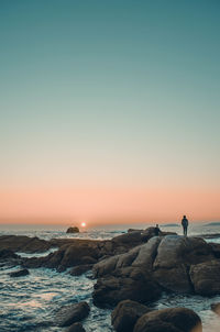 Silhouette man standing on beach against clear sky during sunset