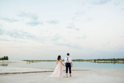 Couple standing at beach against sky