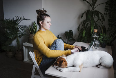 Young woman working on digital tablet while sitting by dog at home