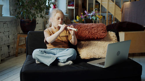 Girl playing flute while sitting on sofa at home