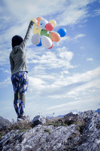 Rear view of woman with balloons standing against sky