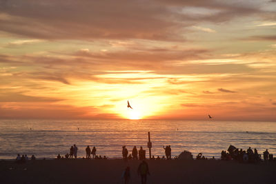 Silhouette people on beach against sky during sunset