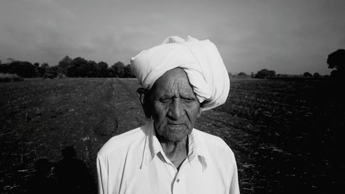 Close-up of senior man wearing turban standing on field against sky