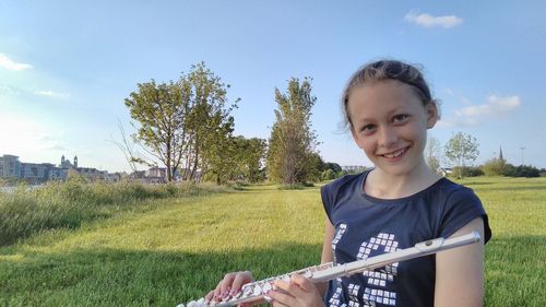 Portrait of smiling woman holding flute while standing on grassy field against sky