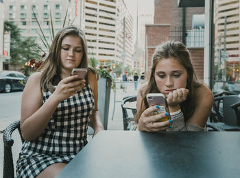 Female friends using smart phones while sitting at sidewalk cafe