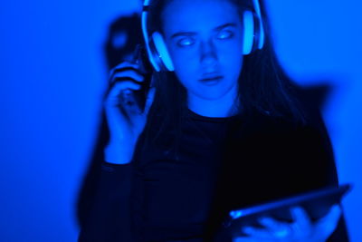 Close-up of young woman listening music against blue background