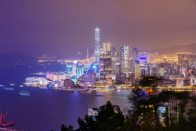 Illuminated buildings by river against sky at night