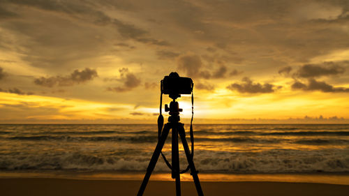 Silhouette camera on beach against sky during sunset