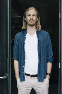 Portrait of confident businessman with hands in pockets at doorway