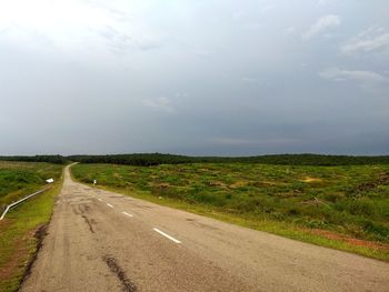 Empty road amidst field against sky