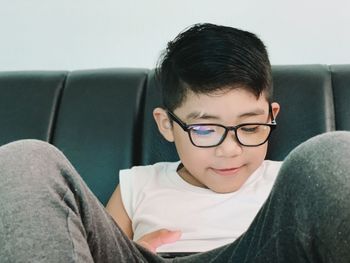 Portrait of teenage boy wearing glasses sitting with a gadget