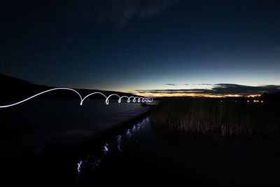 Light trails on bridge over road against sky at night