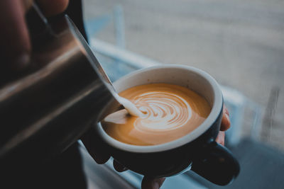 Close-up of hands making froth art coffee on table