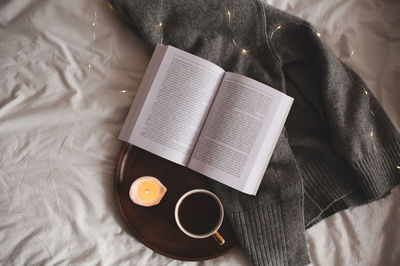 Cup of coffee with leopard print staying on wooden tray with scented burning candle and open book 