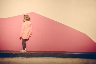 Rear view of woman standing on pink wall against sky