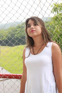 Thoughtful young woman standing against chainlink fence