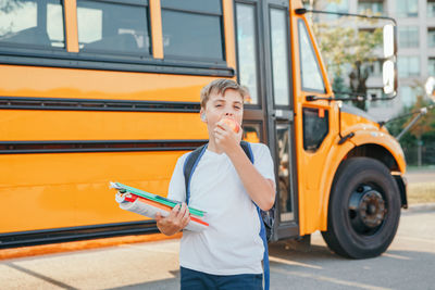 Portrait of boy eating fruit against school bus