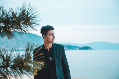 Young man looking away against sky