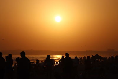 Silhouette people on beach against orange sky