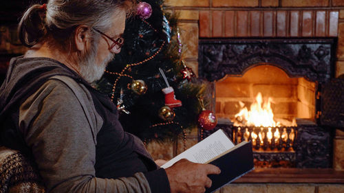 Man reading book while sitting by christmas tree at home