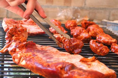 Cropped hand cooking meat on barbecue grill