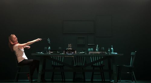 Woman laughing and gesturing while sitting on chair at dining table in darkroom