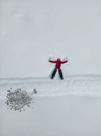 Aerial view of a girl in a red snowsuit playing the angel