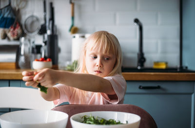 Little blonde girl is helping to prepare dinner in the kitchen.