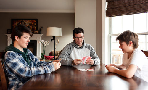 Father and adolescent sons playing cards at the table together.